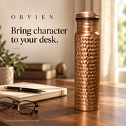 Classic hammered bottle beside a notebook, pen and glasses on a walnut desk.
