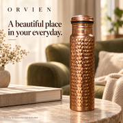 Classic hammered bottle on a pale stone side table near an olive armchair.